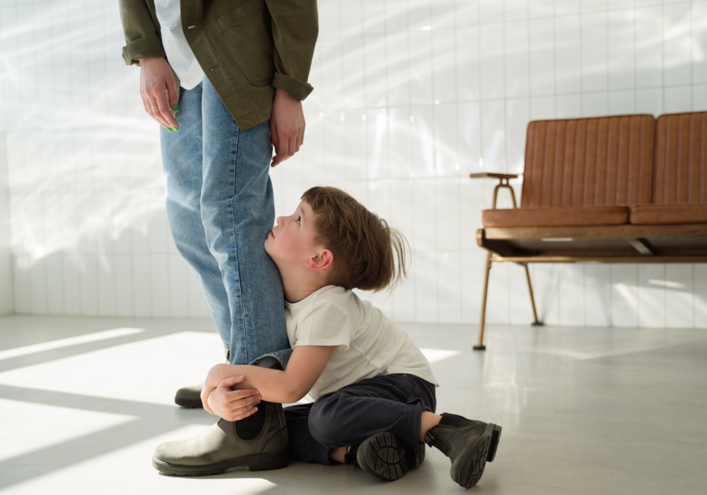 Young boy holding tightly to a parent's leg.